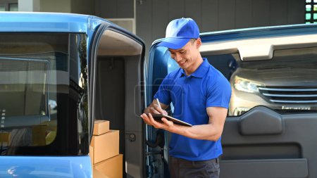 Foto de Hombre de reparto en uniforme azul usando tableta digital junto a la furgoneta de entrega abierta. Concepto de servicio de envío y entrega. - Imagen libre de derechos