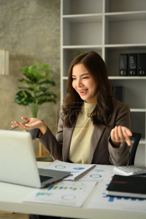 Photo for Friendly asian female entrepreneur talking on video call, consulting client distantly via laptop at workplace. - Royalty Free Image