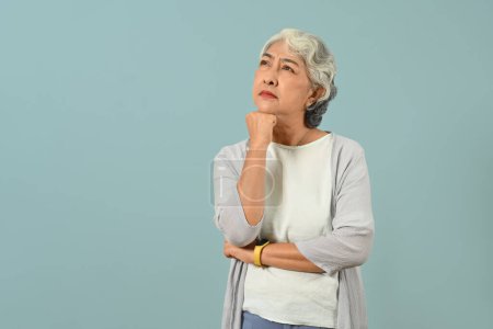 Thoughtful senior woman thinking and looking up expressing doubt and wonder isolated blue background. 