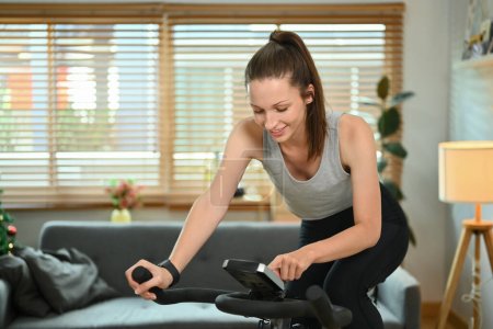 Photo for Beautiful sportswoman working out on on a smart exercise bike at home. - Royalty Free Image