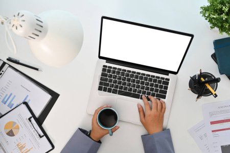Foto de Trabajadora sosteniendo una taza de café y usando un portátil en un escritorio de oficina blanco. Vista superior. - Imagen libre de derechos