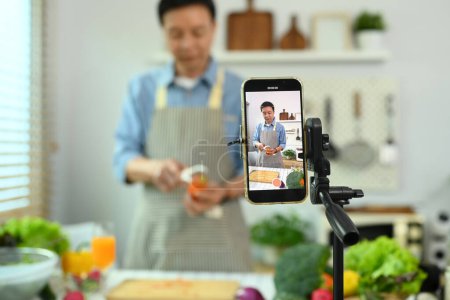 Foto de Hombre de mediana edad grabación de vídeo con receta saludable de batido verde en el teléfono inteligente - Imagen libre de derechos