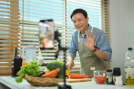Foto de Positivo hombre de mediana edad grabación de vídeo con receta saludable de batido verde en el teléfono inteligente - Imagen libre de derechos