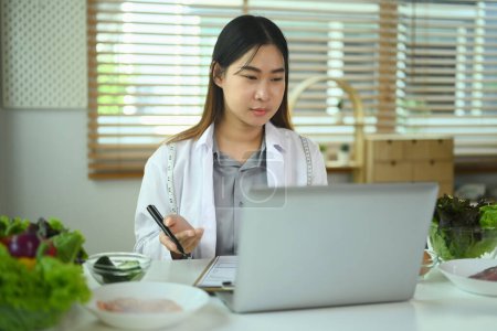 Foto de Retrato de mujer dietista en bata blanca usando laptop para consulta en línea vía video chat con su paciente - Imagen libre de derechos