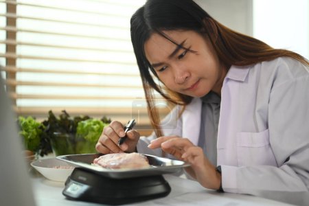Foto de Dietista o nutricionista que pesa pechuga de pollo cruda en una balanza mientras trabaja en un plan de dieta en la clínica - Imagen libre de derechos