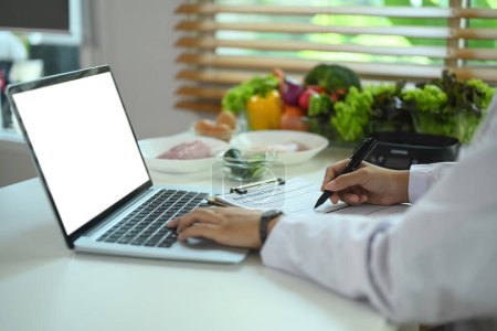 Foto de Primer plano ver nutricionista profesional utilizando el ordenador portátil y receta en el escritorio - Imagen libre de derechos