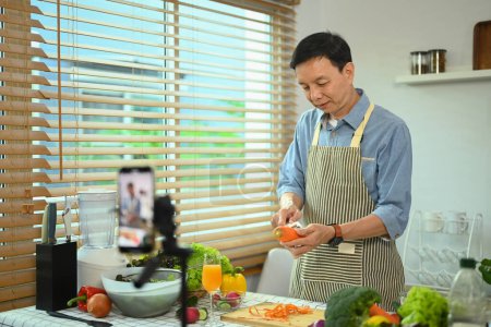 Foto de Hombre de mediana edad activa grabación de vídeo blog sobre la nutrición saludable en el teléfono inteligente en la cocina. - Imagen libre de derechos