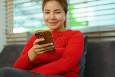 Foto de Mujer joven feliz usando el teléfono móvil en el sofá, pasar el fin de semana tine en casa. - Imagen libre de derechos