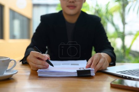 Foto de Joven empresario de traje negro revisando informes financieros en un lugar de trabajo moderno. - Imagen libre de derechos