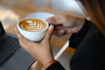 Foto de Primer plano plano de las manos femeninas sosteniendo la taza de café con hermoso arte de café con leche. - Imagen libre de derechos
