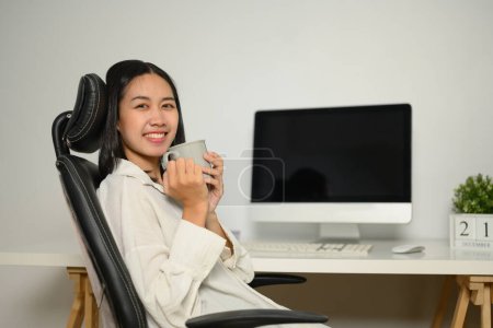 Foto de Atractiva joven empresaria tomando café en el escritorio de la oficina. - Imagen libre de derechos