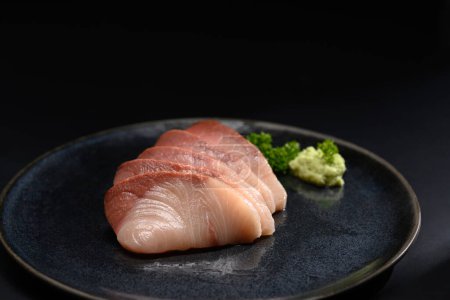 Fresh Hamachi sashimi on black plate with parsley leaf. Japanese food style.