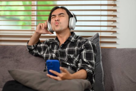 Foto de Feliz joven con auriculares inalámbricos disfrutando de su lista de reproducción de música favorita en el teléfono móvil. - Imagen libre de derechos