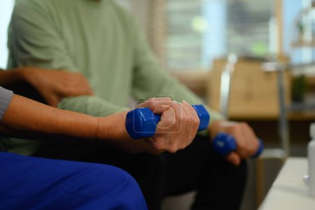 Foto de Enfermera o fisioterapeuta cuidadora que ayuda a un hombre mayor a hacer ejercicio con mancuerna en casa. - Imagen libre de derechos