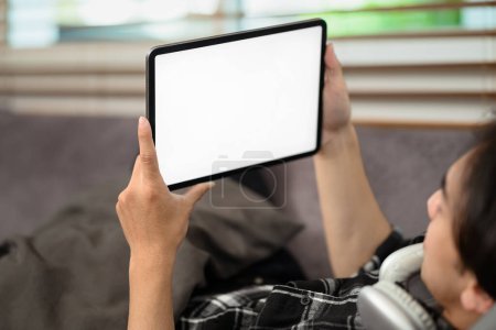 Foto de Hombre sosteniendo tableta digital con pantalla de escritorio en blanco acostado en el sofá. - Imagen libre de derechos
