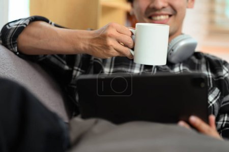 Foto de Sonriendo hombre adulto beber café y navegar por Internet en la tableta digital. - Imagen libre de derechos