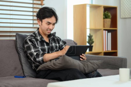 Foto de Hermoso asiático hombre de compras en línea, navegar por Internet en la tableta digital en casa. - Imagen libre de derechos