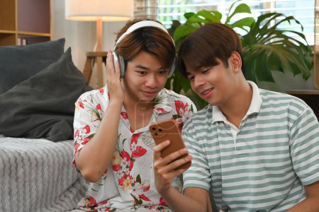 Photo for Loving young gay couple listening music with headphone and smartphone at home. - Royalty Free Image