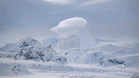 Clouds float above snow mountain ranges. Amazing Antarctic winter nature with snow capped mounts at cloudy day. Climate change and global warming concept at environment scenery of Antarctica