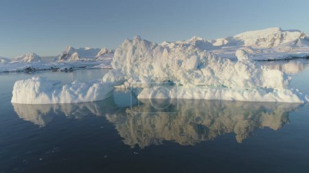 Iceberg Melt in Clear Ocean Water Drone Above View. Huge Ice Float in Reflection Water, Global Climate Warming Concept Pan Left Flight. Winter Polar Glacier Majestic Panorama Footage Shot in 4K UHD