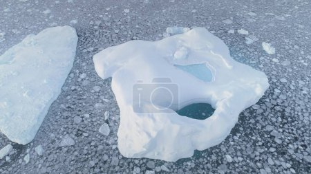 Aerial shot of close-up iceberg with pool. Antarctica zoom in drone flight. Ice mountain among polar ocean. Pieces of ice floating around frozen icebergs. Permafrost. Antarctic continent. 4k footage.