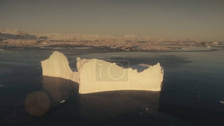 Close-up iceberg. Antarctica aerial drone view flight. Timelapse view from above sunlit iceberg with clear water pool in the ocean, next to the snow covered Antarctic continent shore. 4k footage.