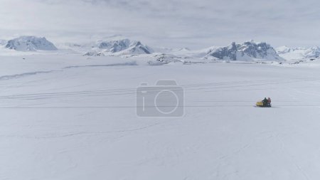 People Riding On Vintage Snowmobile. Aerial Antarctica Flight. Drone Overview Shot Of Snow Covered Land And Mountains. White Winter Landscape. Extreme Outdoor Activity. 4k Footage.