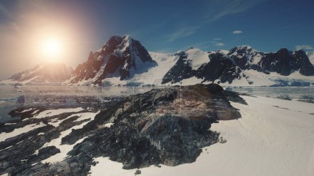Sunset over Antarctica Mountains, Ocean. Lemaire Channel Aerial Flight. Drone Overview Shot Of Mighty Mounts, Snow, Ice Covered Land. Bright Sun Over Ice Cold Ocean. Winter Landscape. 4k Footage.
