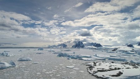 Vuelo aéreo sobre el océano Antártico. Time Lapse. Hyper Lapse. Nubes en movimiento rápido en el cielo. Drone Overview of Icebergs, Ice Pieces Floating In Sunlit Ocean (en inglés). Nieve cubierto montañas poderosas fondo
