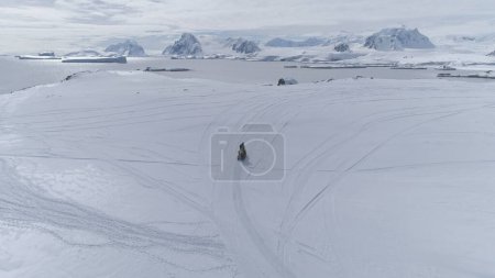 Photo for Aerial Flight Over Fast Moving Snowmobile. Antarctica Landscape. Man Riding On Vintage Ski-doo On Snow Covered Land. Polar Ocean, Mountains Background. Extreme Outdoor Activity. 4k Footage. - Royalty Free Image