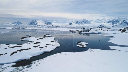 Aerial Flight over Antarctica Vernadsky Base, Snow Shoreline and Ocean (en inglés). Drone Overview of Polar Surface and Ice Frozen Ocean (en inglés). Snow Covered Mighty Mountains Background in Antarctic Land (en inglés). Filmación 4k.