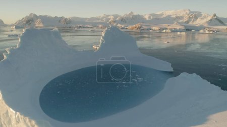 Close-up iceberg pool. Antarctica aerial view drone flight 4k. Slow motion zoom shot the white iceberg with oval blue clear water pool next to the Antarctic continent. Snow covered mountains