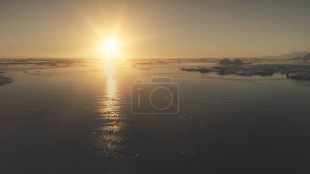 Antarctica ocean sunset light. Aerial drone view flight. Fast hyperlapse shot the bright orange sun over the ocean surface covered ice, snow pieces and icebergs. Flying over the water. Copter shot. 4k