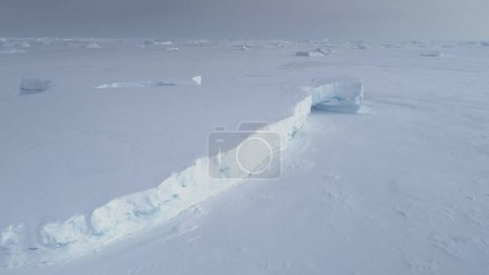 Vue aérienne du champ de glace arctique coincé par un iceberg tabulaire. Snow Covered Antarctica Frozen Lagoon Seascape at Peninsula Coast. Hiver Epic Cold Sea Surface Tracking Top Drone Shot Footage 4K UHD
