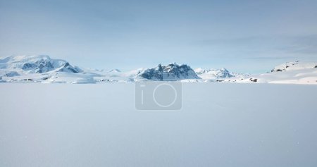 Foto de Invierno Antártida cubierta de nieve paisaje natural. Océano congelado, cordillera de fondo, clima soleado, cielo azul. Tierra blanca del desierto de hielo. Escena de viaje polar ártico. Vuelo en avión no tripulado de ángulo bajo - Imagen libre de derechos