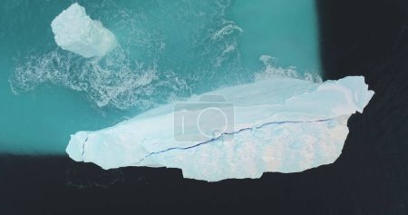 Huge crashed iceberg melting in Antarctica ocean. Glaciers floating in splashing blue water waves, aerial top down view panorama. Environment ecological issue of global warming, climate change