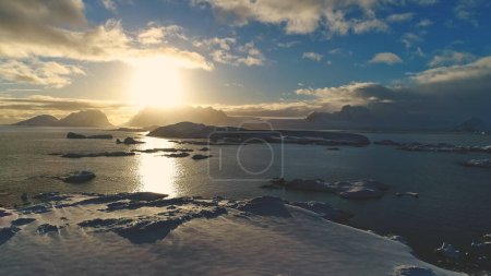 Foto de Puesta de sol sobre la isla de nieve de la Antártida, vista aérea frontal. Reflexión solar sobre el agua del océano en el verano polar antártico. Hermoso cielo horizonte paisaje. Avión no tripulado vuelo adelante - Imagen libre de derechos