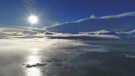 Antarktis-Landschaft. Drohnenflug aus der Luft. Sonnenspur weißer, heller Polarsonne über dem Ozean, bedeckt von leichtem Nebel. Eis- und schneebedeckte Oberfläche des antarktischen Kontinents. Panorama-Übersicht.