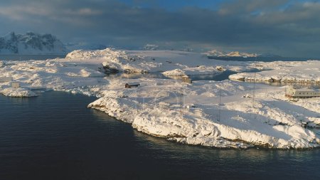 Drohnenblick über der antarktischen Polarstation - der Vernadsky Base. Meeresküste - offene Wasseroberfläche. Schneebedeckte Südpol-Siedlung. Majestätische Landschafts-Luftfahrt