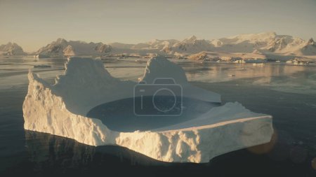 Eisbergbad. Drohnenflug in der Antarktis aus der Luft. Zeitlupe fliegt über den großen Eisberg mit Wasserpool im Polarmeer neben den schneebedeckten Bergen des antarktischen Kontinents.