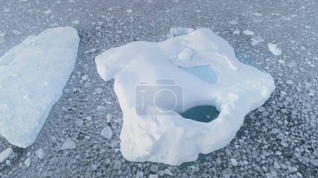 Aerial of close-up iceberg with pool. Antarctica zoom in drone flight. Ice mountain among polar ocean. Pieces of ice floating around frozen icebergs. Permafrost. Antarctic continent.