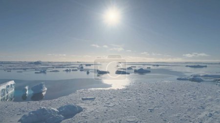 Luftflug über den antarktischen Ozean, Eisberge. Sonnenlicht über dem gefrorenen Wasser. Eisstücke treiben im kalten Ozean. Weiße Polarlandschaft im hellen Sonnenuntergang. Antarktischer Kontinent.