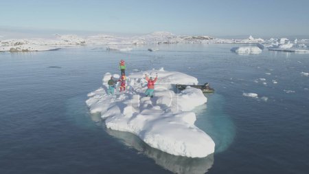 Im ruhigen, eisigen Wasser der Antarktis versammelt sich ein Forscherteam auf einer schwimmenden Eisscholle, umgeben von schneebedeckten Inseln, unter der hellen Weite eines wolkenlosen Himmels..