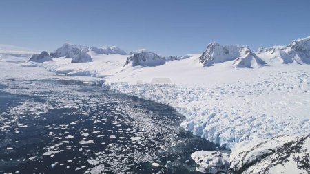 Vuelo aéreo sobre nieve, costa helada de la Antártida. Paisaje de invierno. Trozos de hielo flotando en el océano Polar. Superficie cubierta de nieve de la costa antártica. Silvestre.