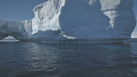 Antarktis-Flug über den Polarmeer zum Eisberg. Erstaunliche Winterlandschaft. Riesiger sonnenbeschienener Eisberg inmitten des kalten antarktischen Ozeans. Massiver Eisberg mit Bogen. Winterlandschaft. Wildnis.