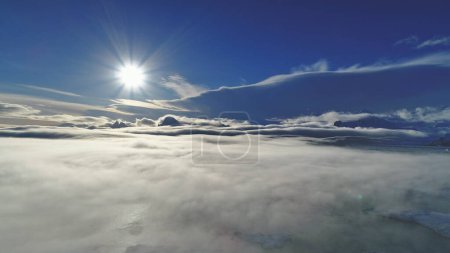 Sol antártico, niebla. Avión no tripulado de visión aérea. Vista general de la Antártida sol blanco brillante por encima de la superficie densa smog que cubre el agua del océano y monta. Increíble panorama invernal. Paisaje polar.