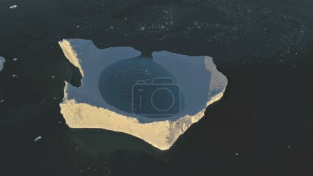 Top down view iceberg. Antarctica aerial drone flight . Slow motion overview large lone sunlit iceberg with clear water pool in the polar ocean water, next to the Antarctic continent. Harsh