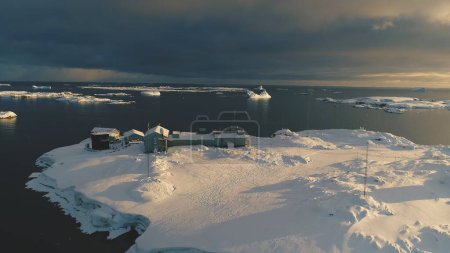 Zeitlupen-Drohnenbild über der antarktischen Polarstation - dem Vernadsky Base. Offene Wasseroberfläche an der Meeresküste. Schneebedeckte Südpol-Siedlung. Erstaunliche Landschafts-Luftfahrt.