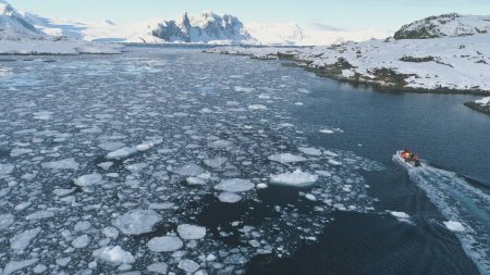 Téléchargez les photos : Zodiac Boat in Antarctica Ocean Aerial tracking. Drone Flight Overview of Antarctic South Pole. Flotteur de bateau en caoutchouc dans le paysage d'eau d'hiver gelé parmi la côte de glace. - en image libre de droit