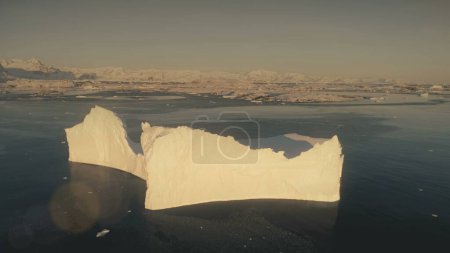 Close-up iceberg. Antarctica aerial drone view flight. view from above sunlit iceberg with clear water pool in the ocean, next to the snow covered Antarctic continent shore.